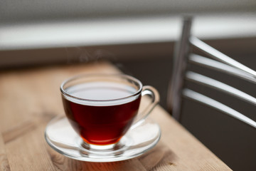 A glass cup of hot black tea on the wooden table. Breakfast concept.