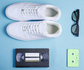 Pop culture, retro style. White hipster sneakers, audio and video cassette, 3D glasses on blue...