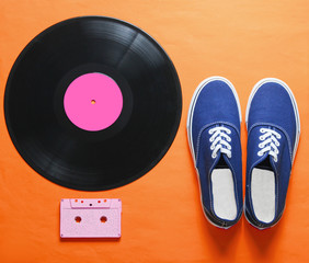 Pop culture. Hipster sneakers, vinyl plate, audio and video cassette, 3d glasses on orange...