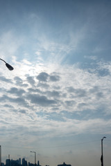 nice day clouds with backlit sun with silhouettes of urban city and street lights