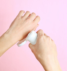 Hand care. Woman holding cream tube and applying moisturizer cream on her beautiful hands for soft hand skin on pink pastel background. Top view, minimalism, flat lay..