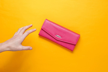 Minimalism trend. Female hand takes pink leather wallet on orange background. Top view.