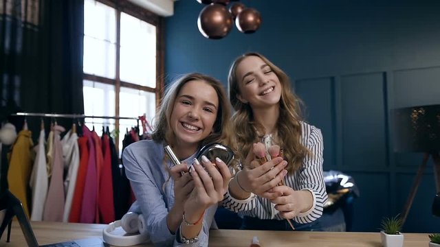 Close up portrait of two handsome women holding make up tools in the hands and possing to the camera.