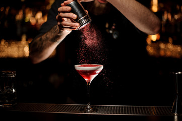 Professional bartender adding to a cocktail with a whipped cream a pink powder