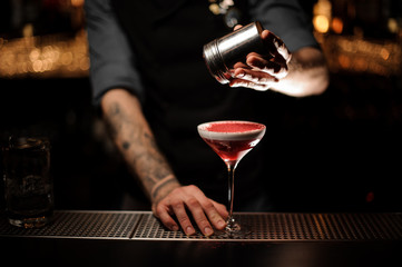 Bartender adding to a cocktail with a whipped cream a pink powder