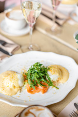 Egg Benedict with little salad on the plate with salmon and arugula. Two eggs delicious hollandaise sauce. Light morning Breakfast on table in restaurant.