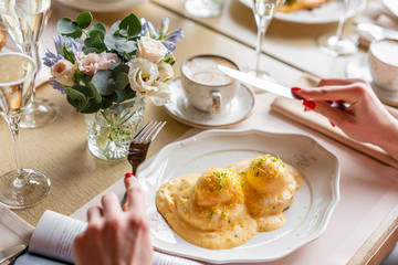 Close up Woman eats Egg Benedict on warm toast brioche. Two eggs delicious hollandaise sauce. Light morning Breakfast on table in restaurant.