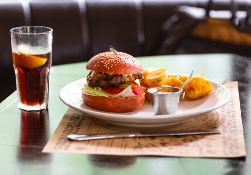 on a white plate, a meat burger with onion, tomato, lettuce and a salted cucumber, french fries and sauce