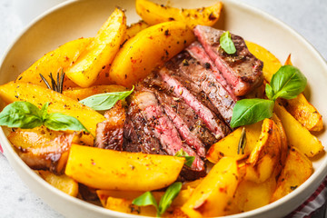 Grilled beef steak with potatoes and basil in a white plate on white background.
