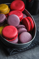 Colored macaroons in metal dish, dark background.