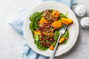 Vegan salad with lentils, pumpkin and dried tomatoes in white plate.