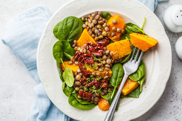 Vegan salad with lentils, pumpkin and dried tomatoes in white plate.
