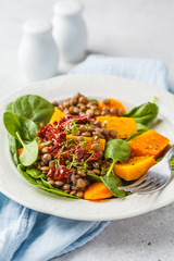 Vegan salad with lentils, pumpkin and dried tomatoes in white plate.