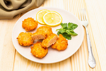 Homemade red fish cakes with lemon and parsley in ceramic plate. With fabric drapery and fork on wooden background, close up.