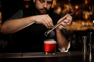 Professional bartender adding to a red cocktail in the glass a grated nutmeg