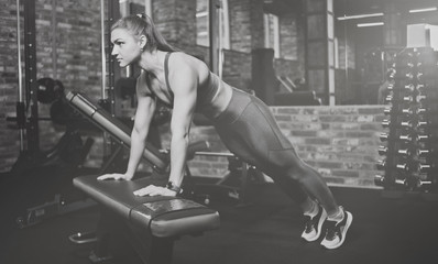 Fototapeta na wymiar Athletic attractive woman wrung out from the bench in gym. Training concept, sport, workout process. Black and white photo