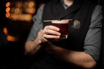 Professional bartender serving decorated cocktail with a one red berry on a skewer
