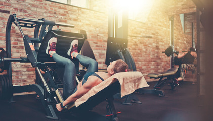 Sportswoman flexing muscles on leg press machine in gym. The training process, legs workout,...