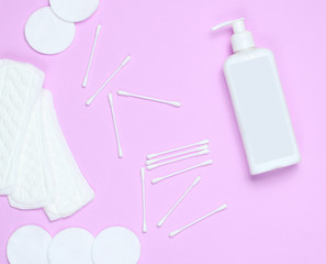 Hygiene products on a pink pastel background. Cotton pads, women's pads, bottle of cream, cotton ear sticks. Top view, flat lay, copy space.