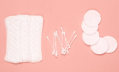 Hygiene products on coral color pastel background. Cotton pads, women's pads, cotton ear sticks. Top view, flat lay.
