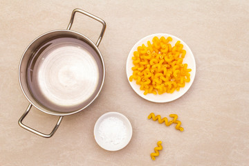 Raw fuzilli with water in pot and salt. Traditional Italian pasta in white plate on stone background. Preparing for children, top view