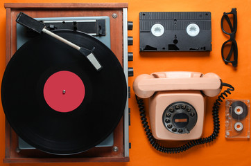 Old-fashioned objects on orange background. Retro style, 80s, pop culture. Top view. Vinyl player,...