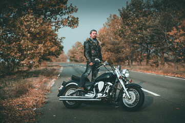 Obraz na płótnie Canvas Stylish biker posing with motorcycle on the road.