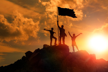 People on top of the mountain with a flag on the background of the evening sky. success,...