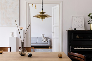 Stylish scandi interior of home space with design wooden table, chairs, sofa and gold pendant lamp....