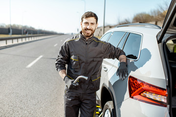 Portrait of a handsome road assistance worker in uniform standing near the broken car on the highway