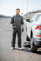 Portrait of a handsome road assistance worker in uniform standing near the broken car on the highway
