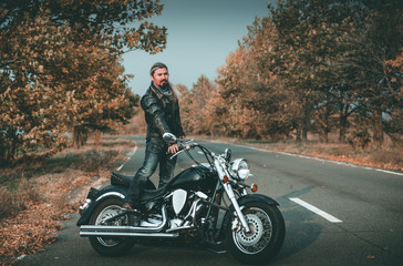 Stylish biker posing with motorcycle on the road.