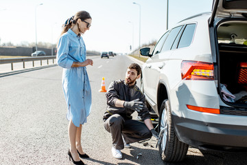 Road assistance worker helping young woman to change a car wheel on the highway