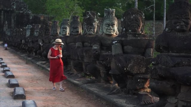 Attractive young woman walking through the temple morning. Ancient statues on South Gate bridge of Angkor Thom temple.