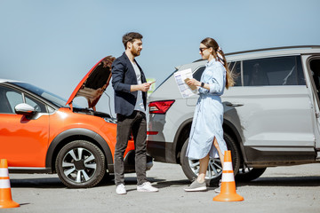 Man and woman arguing, standing together on the road with their cars on the background after the...