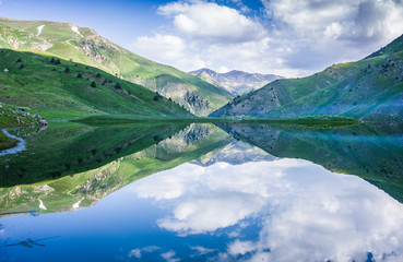 Naklejka na ściany i meble Mountain lake Susyngen, Kazakhstan. Reflection of clouds, green coasts and the blue sky in a surface of the water. 