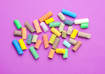 Many colored pastel crayons on a purple background. Top view
