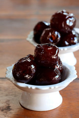 Sweet Jujube or Chinese red date in syrup in white Thai style cup on wood table and space for write wording, Clever idea for fresh fruit preservation, popular sweet, unhealthy food cause of disease