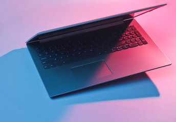 Modern laptop with vibrant gradient pink  blue holographic color lights. Minimal office surrealism concept. - obrazy, fototapety, plakaty
