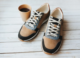 A pair of suede sneakers on a grunge wooden background and a paper cup of coffee. The concept of energy drink, sports shoes and thirst.