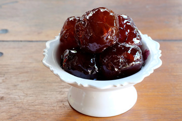 Sweet Jujube or Chinese red date in syrup in white Thai style cup on wood table and space for write wording, Clever idea for fresh fruit preservation, popular sweet, unhealthy food cause of disease