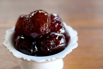 Sweet Jujube or Chinese red date in syrup in white Thai style cup on wood table and space for write wording, Clever idea for fresh fruit preservation, popular sweet, unhealthy food cause of disease