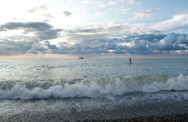 Young female paddling on SUP board in the sea at amazing dark sunset and waves. Sup surfing woman...