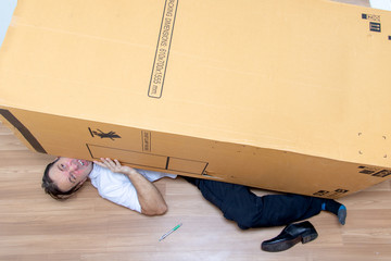 The unhappy man lying under a big box. Large cardboard fall down at the postman.