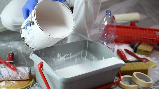 Caucasian house painter worker in white overalls, prepares the white paint to paint the wall with the roller. Construction industry. Footage.
