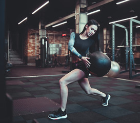 Cheerful brunette woman in sportswear doing exercise with medicine ball at gym.