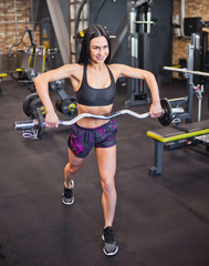 Fototapeta na wymiar Cheerful purposeful brunette athlete doing exercise with barbell in the hands of the gym.