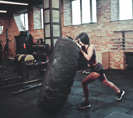 Naklejka na ściany i meble Functional training concept. Strong young brunette woman pushing a heavy wheel in the gym.