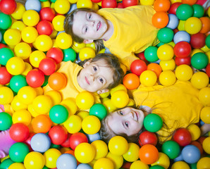 Fototapeta na wymiar Three happy little kids girls in ball pit smiling happily at camera while having fun in children play center. Top view