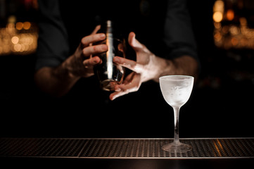 Bartender holding a steel shaker on the foreground of glass
